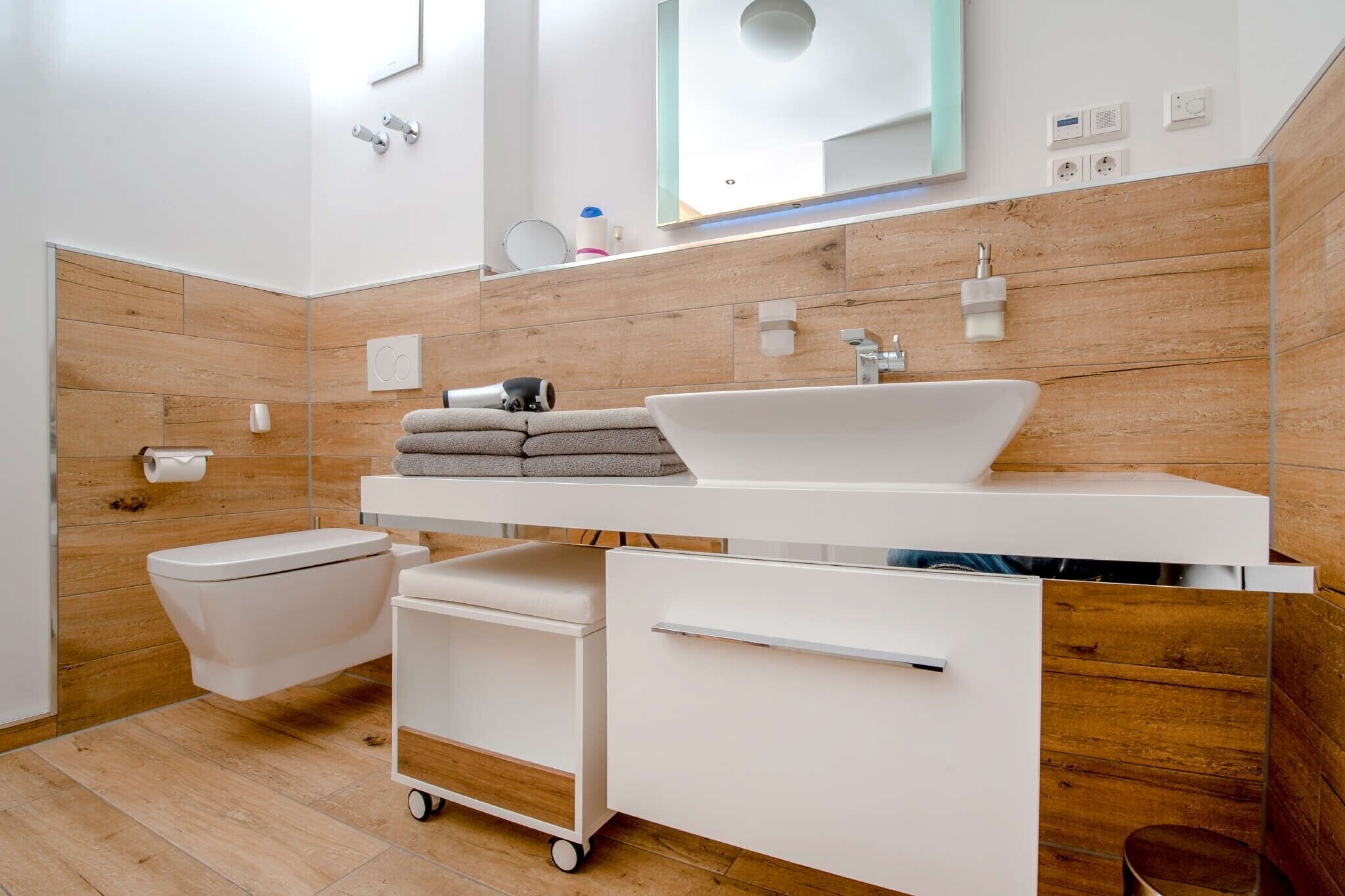 A modern bathroom with a white sink, wooden wall paneling, a toilet, and a cart with towels.