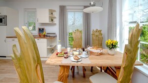 Eine moderne Küche mit weißen Schränken, einem Esstisch, der mit Frühstücksgebäck gedeckt ist, und Blick ins Grüne.