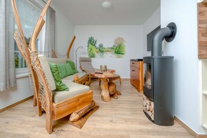 Et hyggeligt rum med en træsofa, et lille bord, en hængekøjsstol og en brændeovn.