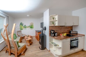 Et moderne køkken med en brændeovn, hvide skabe og et spiseområde med et træbord og stole.