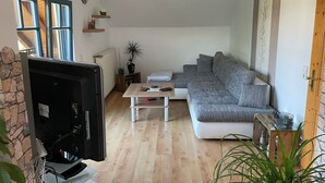 Ein Wohnzimmer mit einer Couch, einem Couchtisch, einem Fernseher und einer Zimmerpflanze.