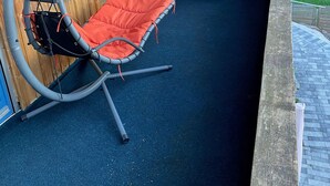 Ein überdachter Sitzbereich im Freien mit einer Schaukel, einer Couch und einem Tisch.