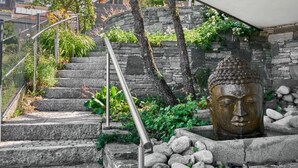 Kivestä rakennettu portaikko, jossa on metallinen kaide, Buddha-patsas ja kasvillisuutta kasvava kivimuuri.