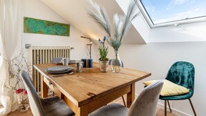 Un comedor con una mesa de madera, sillas, un jarrón con plantas, un radiador y un tragaluz.