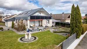 Una casa moderna con techo inclinado, un porche cubierto y un jardín cuidado.