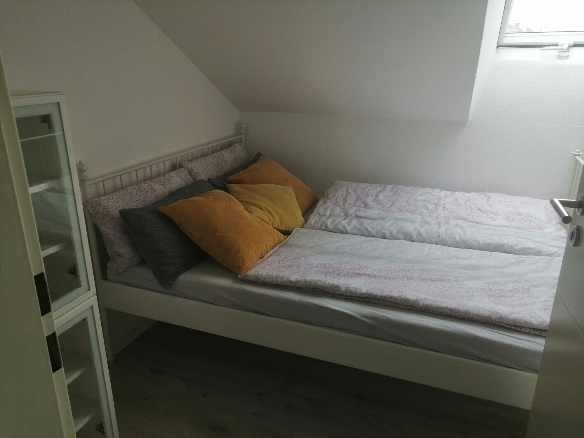 A single bed with a headboard, a bedside table, and a window.