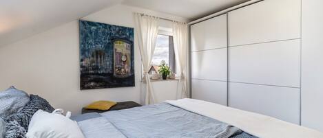 Un dormitorio con cama, un cuadro, una ventana con cortinas y vistas al exterior.
