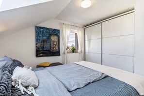 Une chambre à coucher avec un lit, un tableau, une fenêtre avec des rideaux et une vue sur l’extérieur.