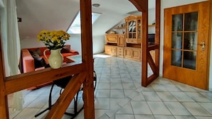 Una habitación con un armario de madera, un sofá, un jarrón con flores y suelo de baldosas.