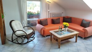 Una sala de estar acogedora con un sillón mecedor, sofá naranja y una mesa de centro con un jarrón de flores.