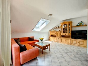 A living room with a sloped ceiling, a sofa, a coffee table, a cabinet, and a television.