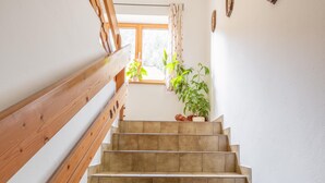 Una escalera con barandas de madera y baldosas color crema, que conduce a una habitación con ventana y plantas en macetas.