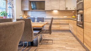 Una cocina moderna con armarios de madera, horno empotrado y comedor con mesa y sillas.