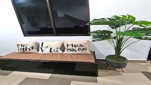 Een zwarte bank met drie kussens, elk met een ander tekstdessin. Een grote potplant staat rechts van de bank.