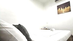 Een slaapkamer met een bed, een kussen, een nachtkastje, een lamp en een aan de muur hangend schilderij.
