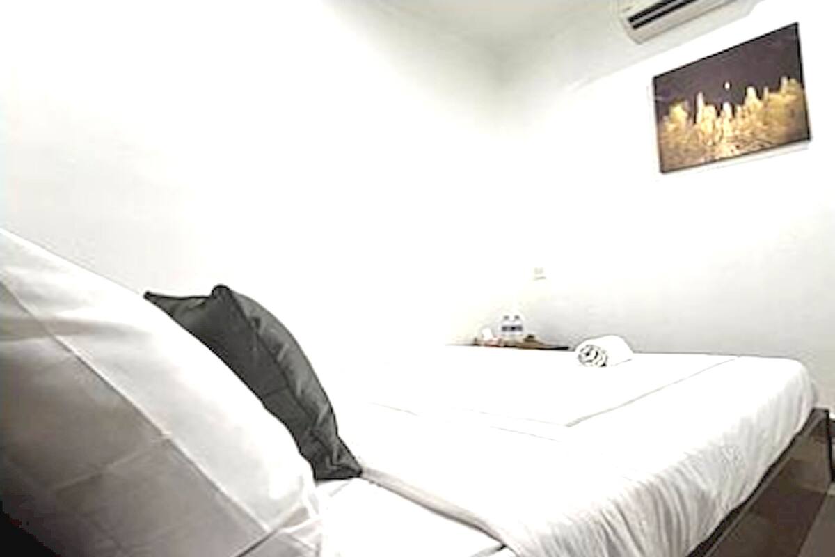 Ein Schlafzimmer mit Bett, Kissen, Nachttisch, Lampe und einem Wandbild.