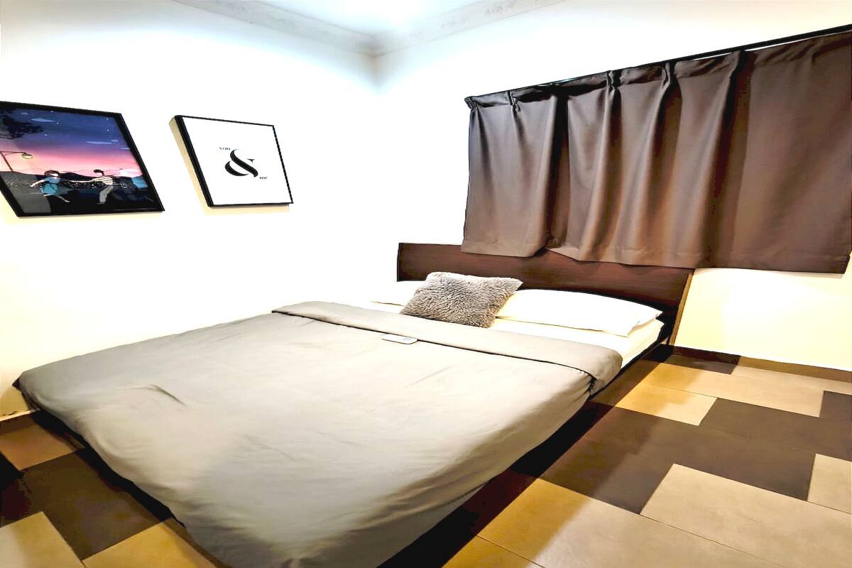 Ein ordentlich bezogenes Bett mit Kissen, ein an der Wand befestigter Bilderrahmen und ein Fenster mit Vorhängen.