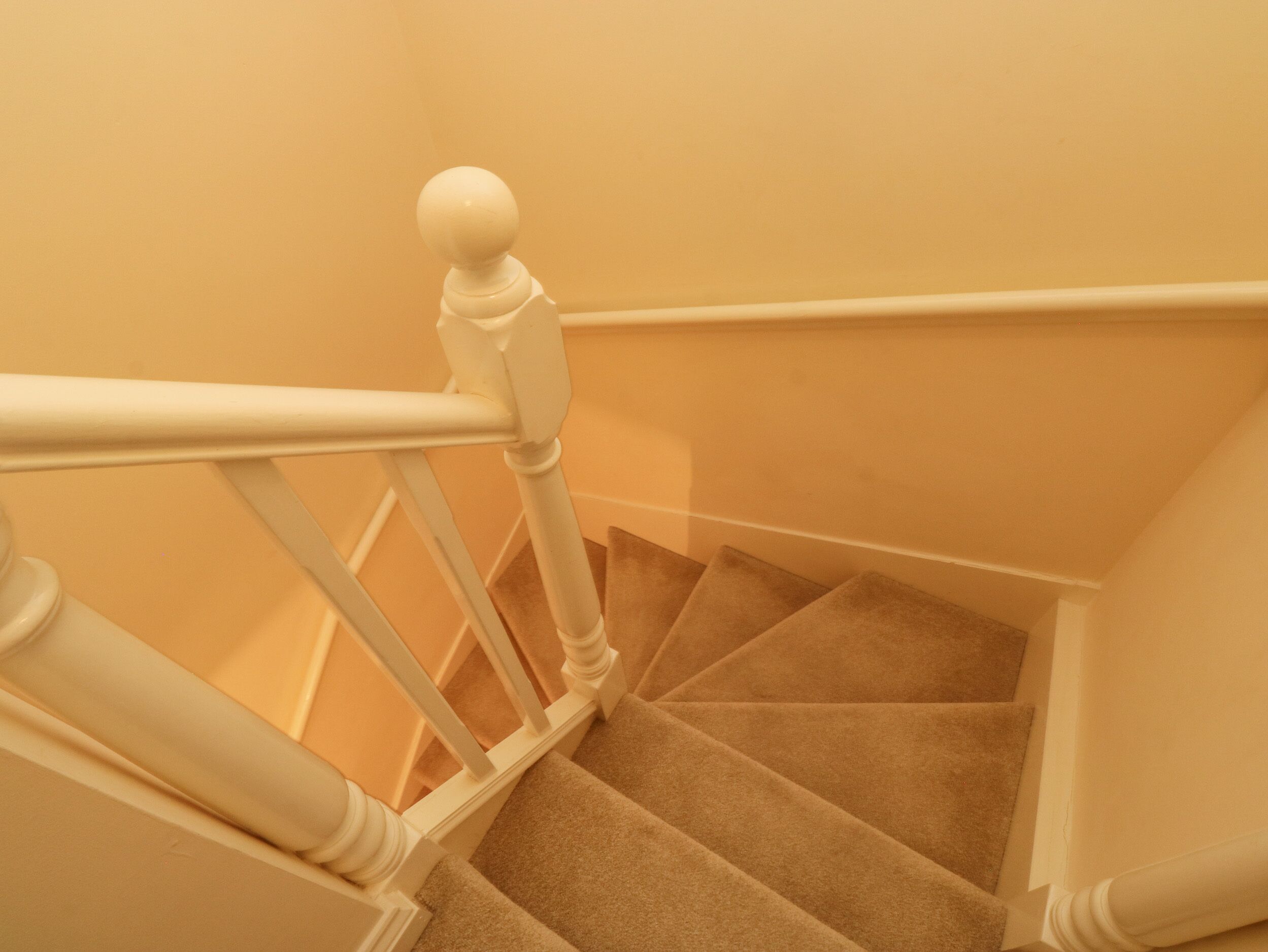 A staircase with white balusters and a beige carpet.