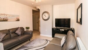Ein modernes Wohnzimmer mit einer Sofagarnitur, einem Fernseher und einer dekorativen Wanduhr.