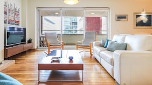 A modern living room with a flat-screen TV, two armchairs, a white sofa, and a wooden coffee table.