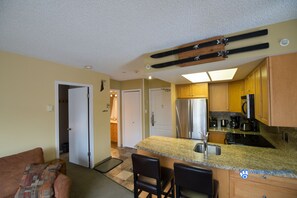 A compact kitchen with a refrigerator, stove, and bar stools.
