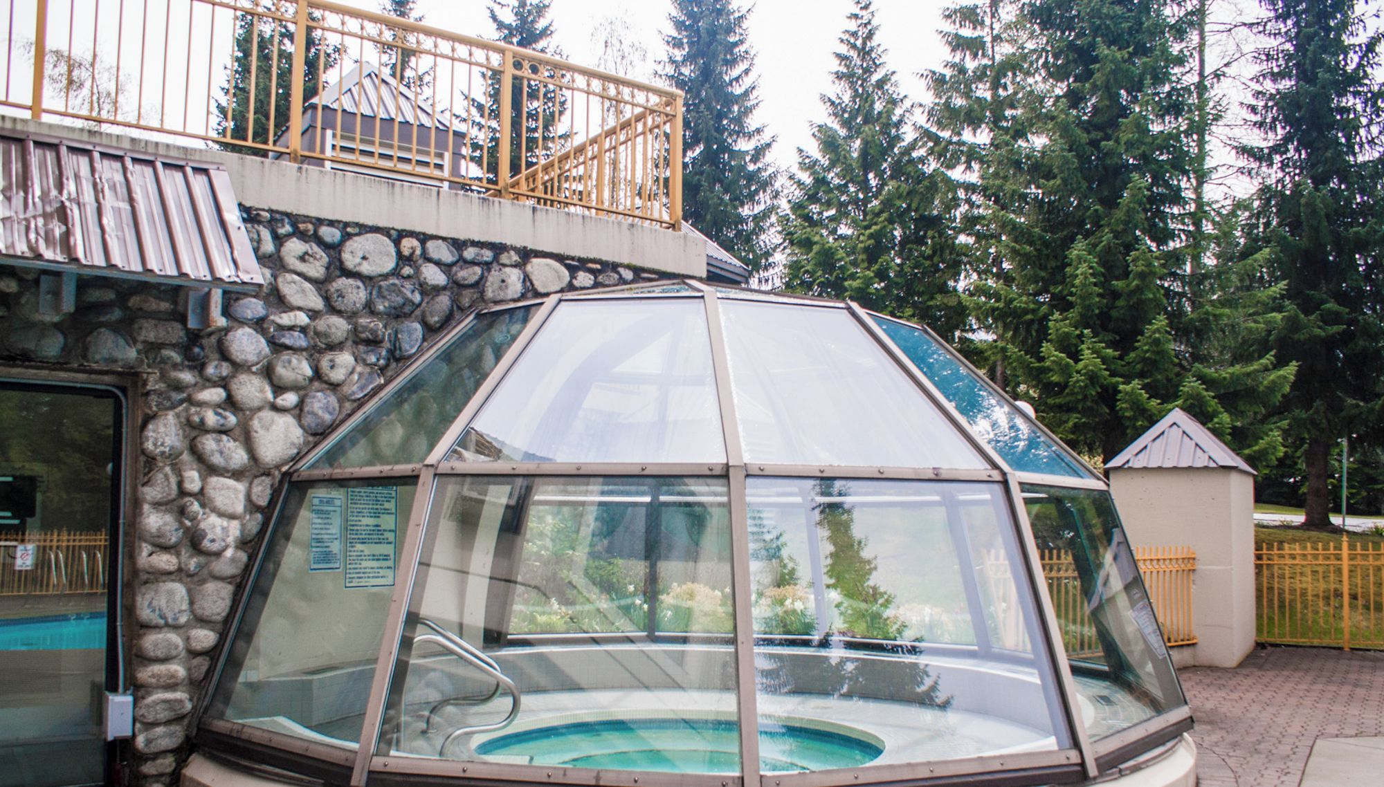A glass-enclosed hot tub with a stone wall and metal railing.