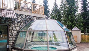 Un jacuzzi entouré de parois en verre, avec un mur en pierre et une balustrade en métal.
