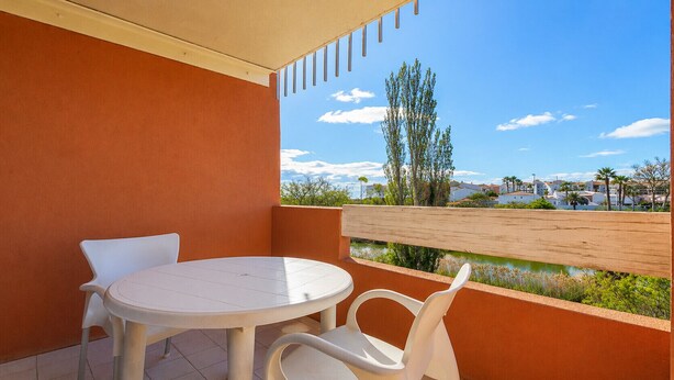 Un balcon avec une table ronde et deux chaises, une clôture en bois et une vue sur une ville côtière.