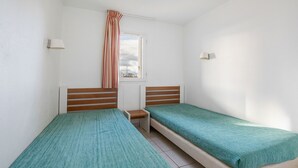 Un petit logement composé d’une seule pièce, avec deux lits simples, une fenêtre donnant sur le ciel et un rideau.