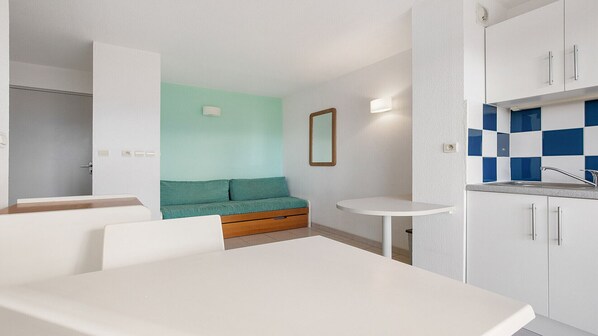 Ein modernes, kompaktes Zimmer mit Küchenzeile, einer kleinen Essecke und einem blaugrünen Sofa.