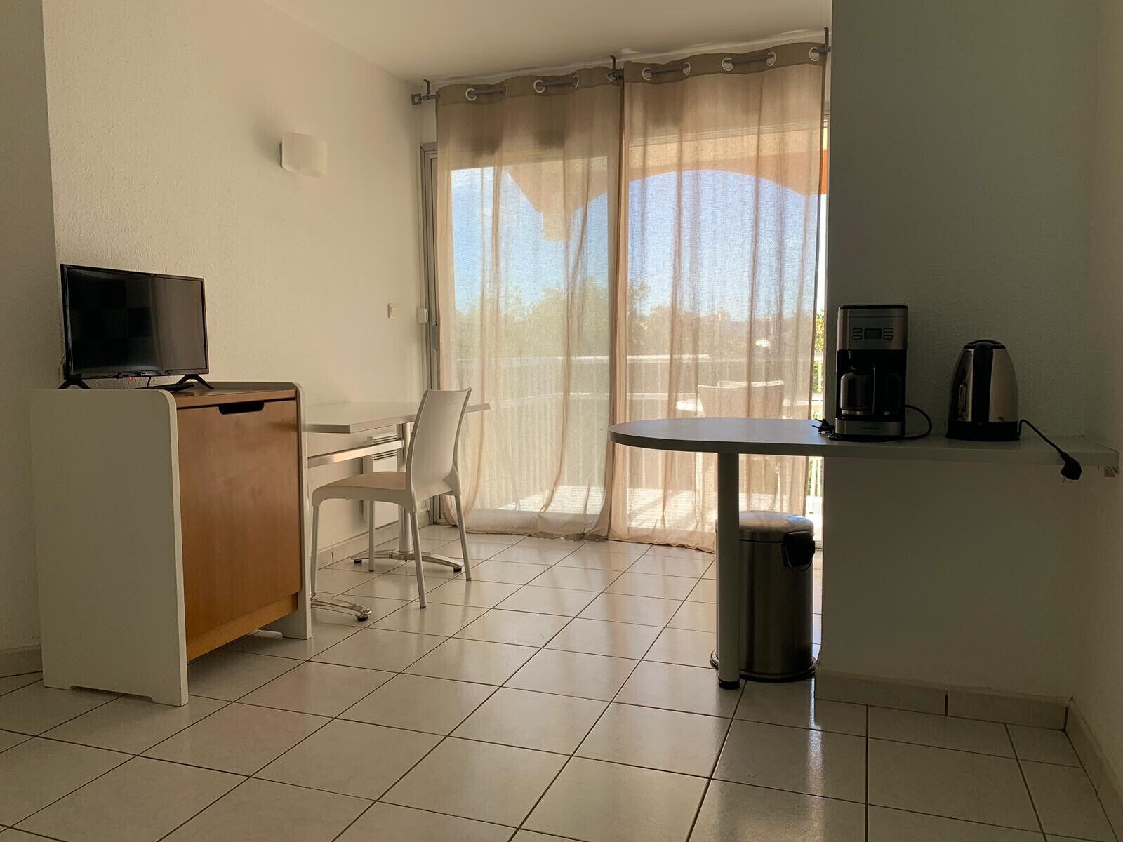 Une pièce comprenant un bureau, une chaise, un téléviseur, une machine à café et une poubelle.