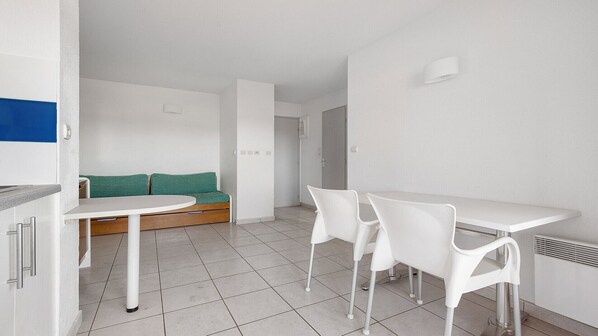 Quarto minimalista com mesa branca, duas cadeiras brancas, sofá verde e radiador branco.
