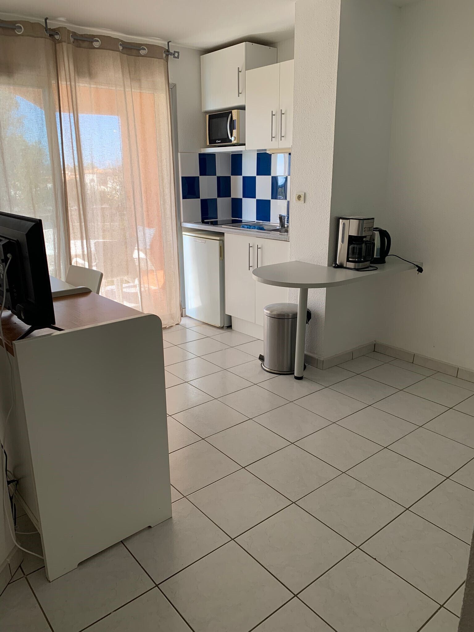 A compact kitchen with a refrigerator, microwave, coffee maker, and a small table.