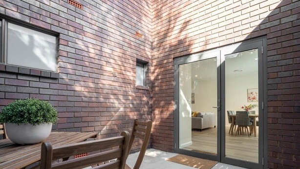 Een terras met een houten tafel en stoelen, een potplant en een bakstenen muur.