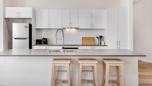 Een moderne keuken met witte kastjes, een roestvrijstalen koelkast, een spoelbak en drie houten krukken.