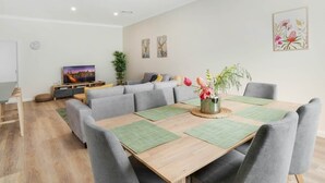 Een moderne woonkamer met een houten eettafel, grijze banken en een televisie.