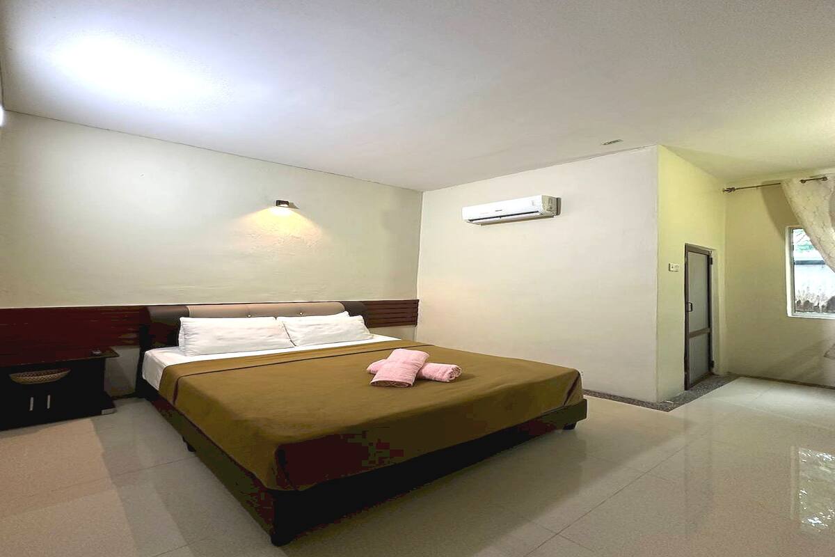 Habitación de hotel con cama, mesita de noche, unidad de aire acondicionado y ventana con cortinas.