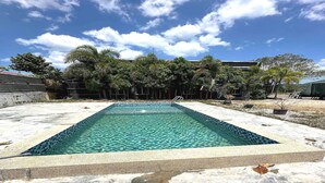 Ein rechteckiger Swimmingpool mit klarem, blauem Wasser, umgeben von einer Betonplattform mit vereinzelten Blättern.