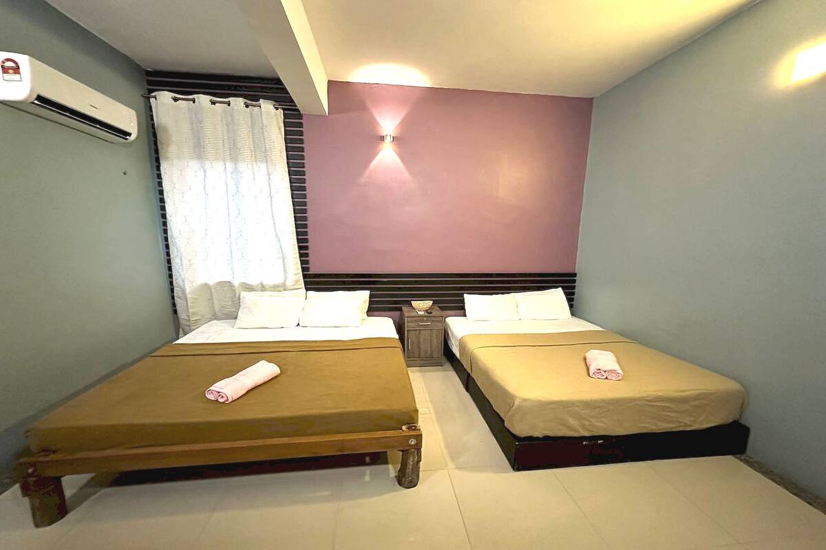 Habitación con dos camas, una mesita de noche, aire acondicionado de pared y una ventana con cortinas.