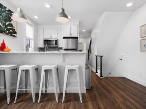 A modern kitchen with white cabinetry, stainless steel appliances, and a wooden floor. - Downtown TC Condo w/ Rooftop + Walk to Beach (Traverse City)