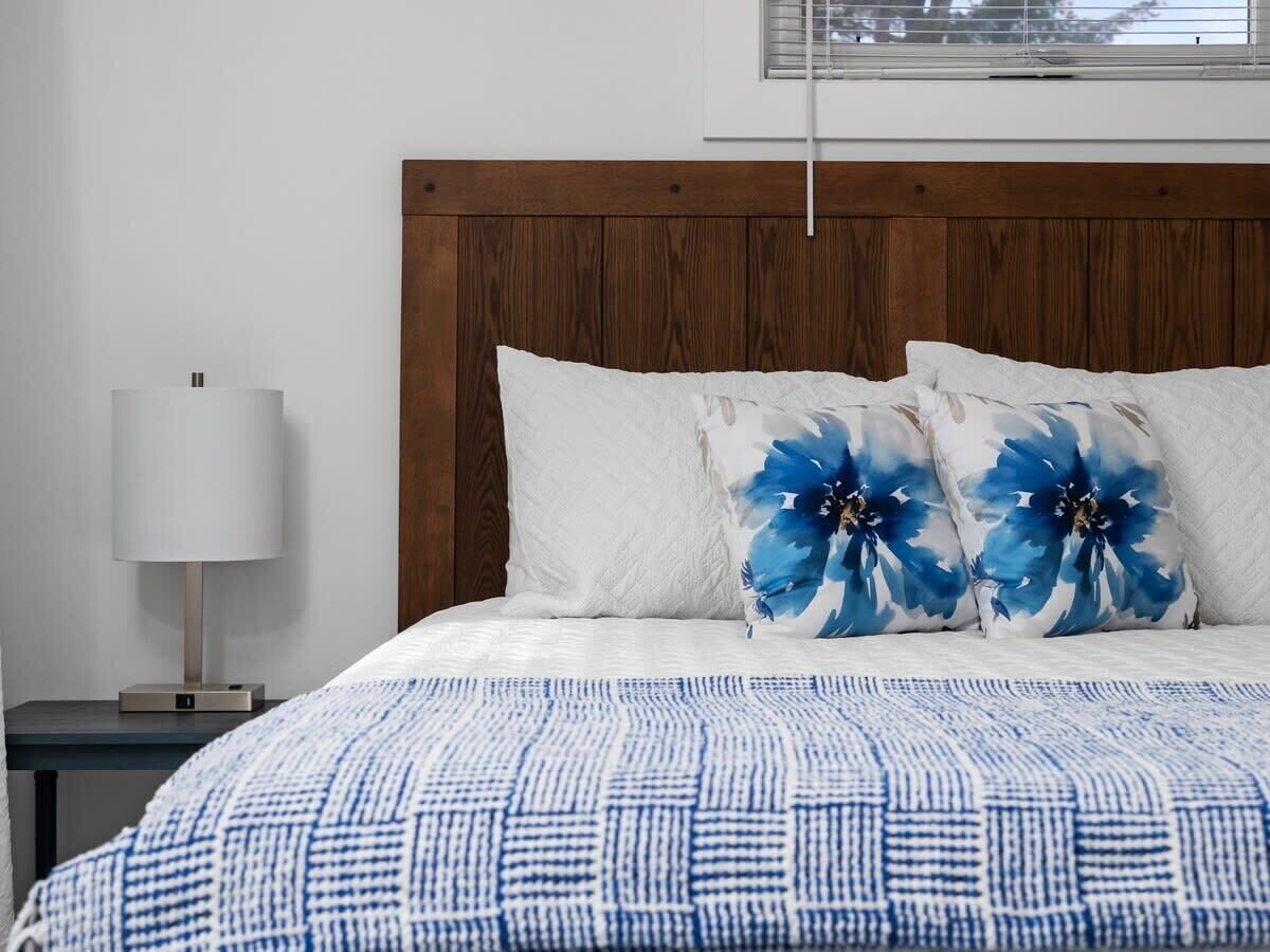 A neatly made bed with a blue and white patterned bedspread, two blue floral pillows, a white pillow, and a wooden headboard.