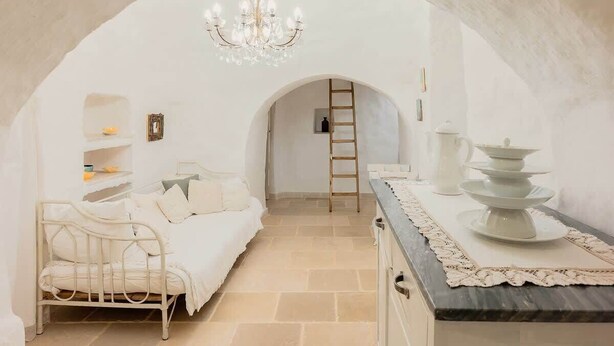 Ein gemütliches Schlafzimmer mit einem weißen Bett, einer Chandelierleuchtre und einem Essbereich mit weiß gedecktem Tisch.