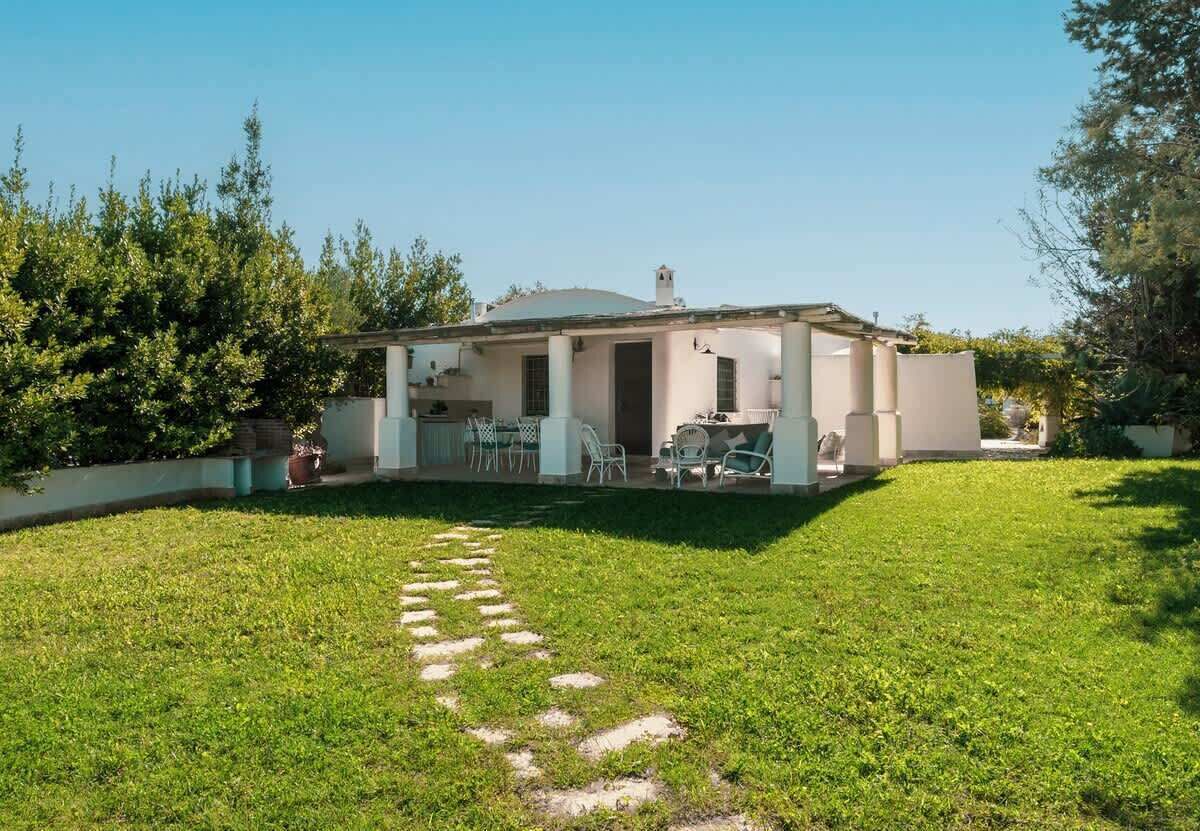 Ein Bungalow mit überdachter Terrasse, einem Rasen und einem Kiesweg, der zum Eingang führt.
