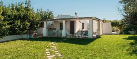 Ein Bungalow mit überdachter Terrasse, einem Rasen und einem Kiesweg, der zum Eingang führt.