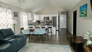 A modern kitchen with white cabinets, a stainless steel refrigerator, and a dining area with a table and chairs.