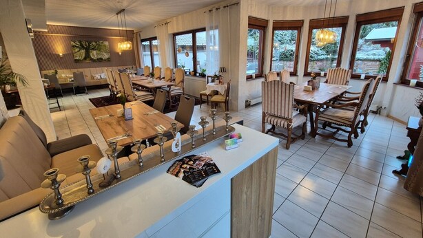Een ruime eetruimte met meerdere tafels en stoelen, een centraal gelegen bar en grote ramen voor natuurlijk licht.