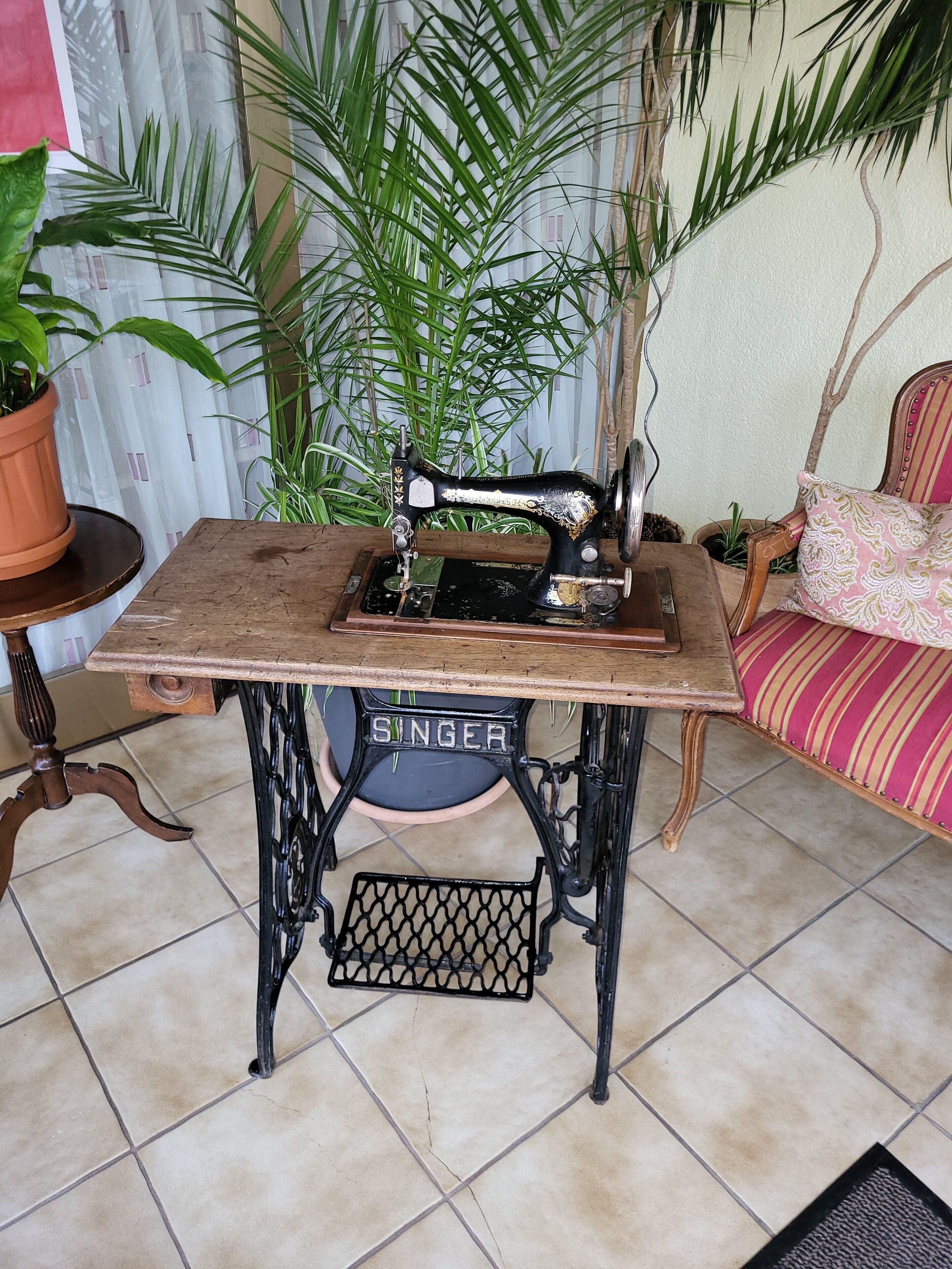 Une machine à coudre Singer posée sur une table en bois, sur un sol carrelé.