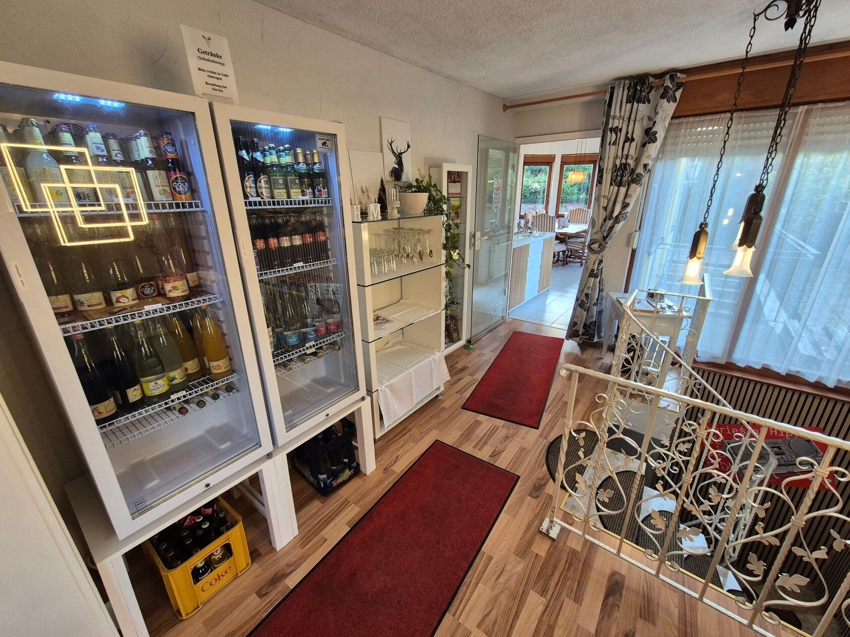 A room with a minibar, a glass door leading to a dining area, and a decorative metal railing.