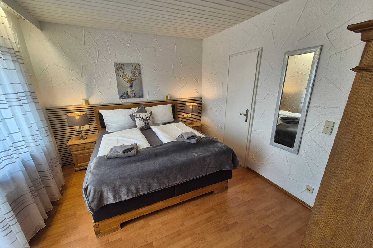 Ein Schlafzimmer mit einem Bett, Nachttischlampen, einem Spiegel und einem Bild an der Wand.