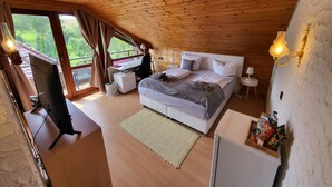 Een slaapkamer met een houten plafond, een bed met kussens, een bureau met stoel, een klein tafeltje en een nachtkastje.